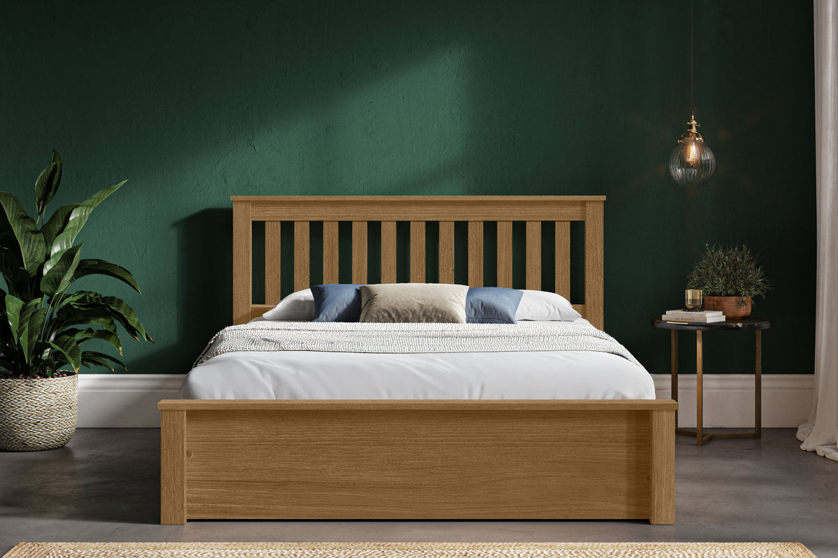 Wooden bed in a room with a green wall and a small table with a plant.