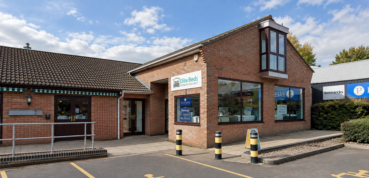 A brick bed shop in Thatcham, with large glass windows, a tiled roof, and a paved parking lot with yellow handicap symbols in the foreground. A blue sign on the right reads PAVES.